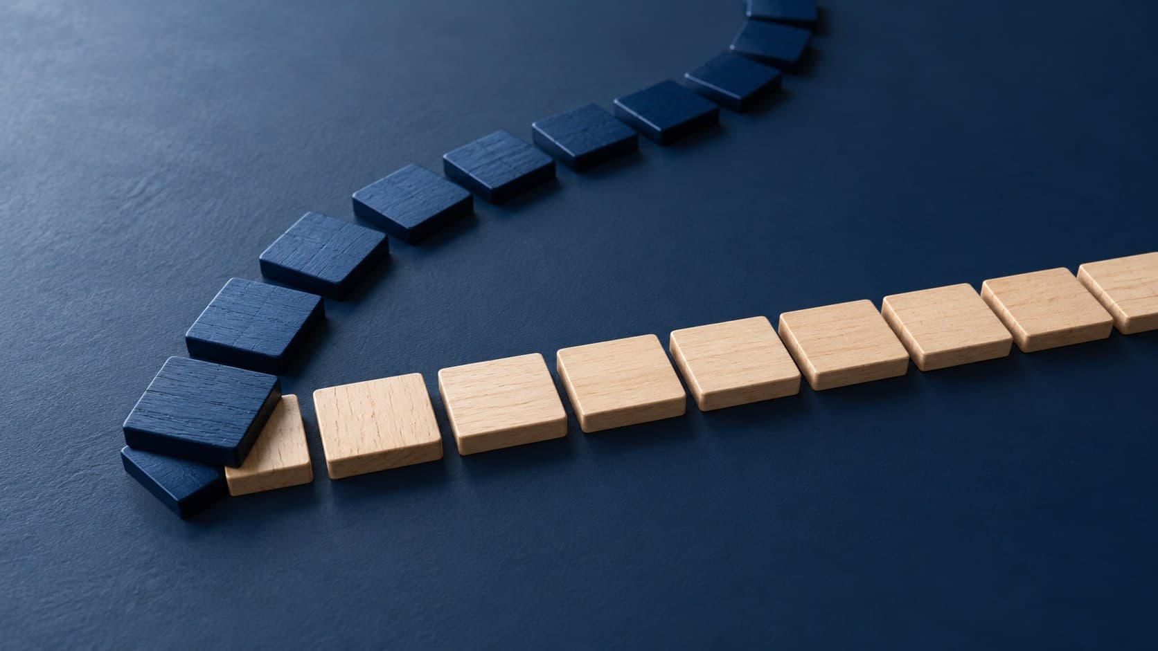 A straight row of pale wooden tiles separates from a curved row of navy tiles on a dark blue surface.