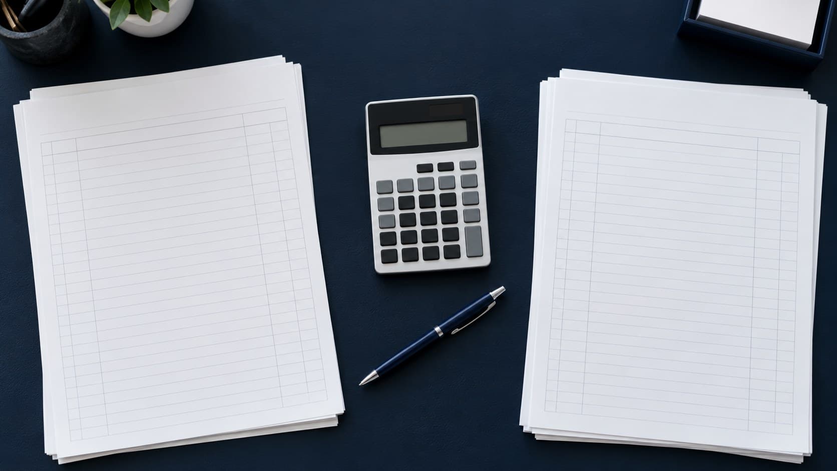 Two blank ledger stacks and a calculator on a navy desk, arranged for a reconciliation check.