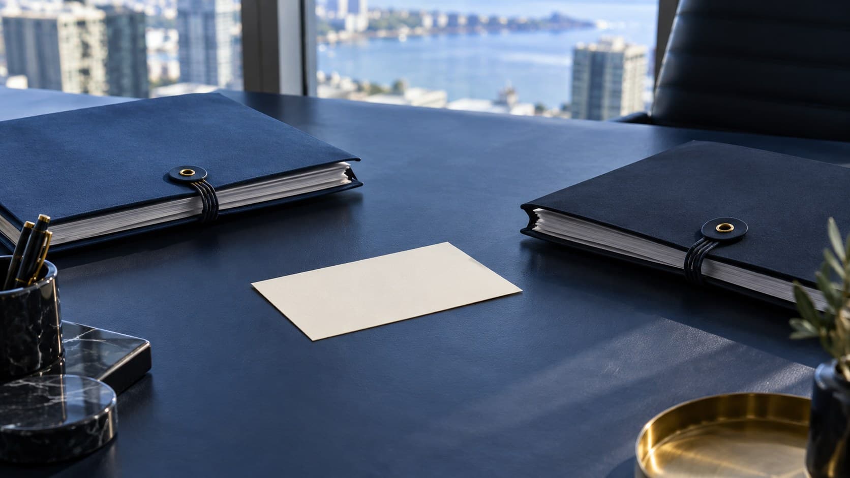 Two unmarked navy document folders face one another across a desk with a blank card between them.