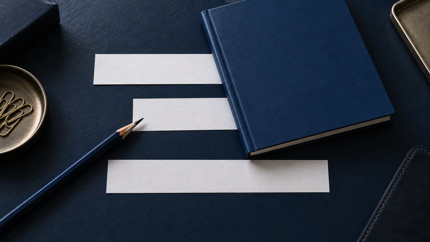 Three blank paper strips lie on a navy desk, their ends partly hidden by a blue notebook, with a pencil beside the middle strip.